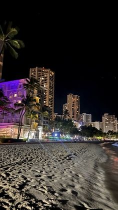 the city lights shine brightly in the night sky over an empty beach and palm trees