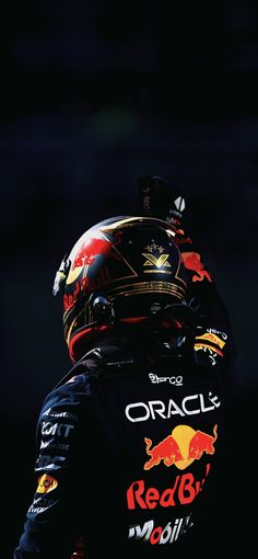 a man in a red bull racing suit with his helmet on and back turned to the camera