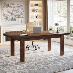 a wooden desk with a laptop on it in front of a window and a rug