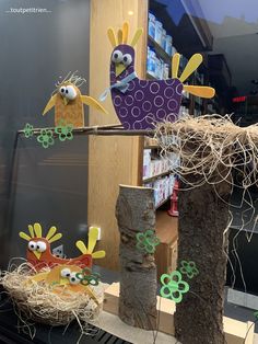 some paper birds are sitting on sticks in front of a store window with hay and flowers