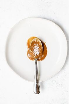 a spoon with some food on it sitting on top of a white plate next to a fork