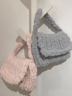 two crocheted purses hanging on the wall next to each other, one pink and one gray