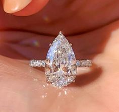 a woman's hand holding an engagement ring with a pear shaped diamond