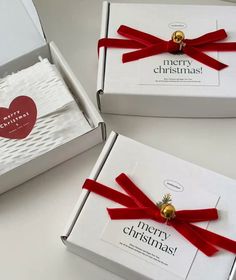 two white boxes with red ribbon and gold bells on them, one is open to show the inside of the box