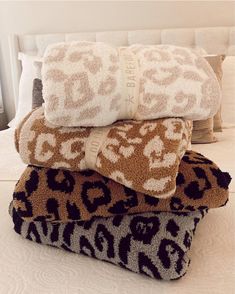 four towels stacked on top of each other in front of a bed with white sheets and pillows