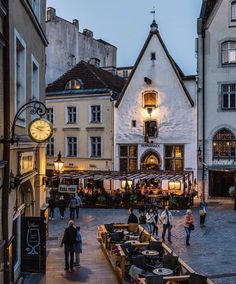 people are walking around in an old town square at dusk, surrounded by buildings and cobblestone streets