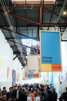 a large group of people are standing in a building with signs hanging from the ceiling