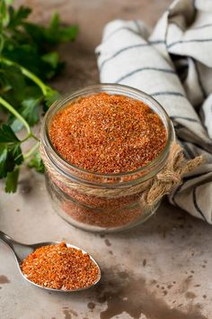 a jar filled with spices next to two spoons on top of a cloth covered table