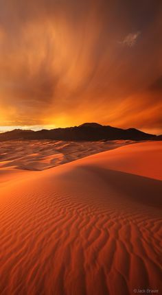 the sun is setting over sand dunes with mountains in the distance