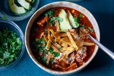 a bowl of chili soup with tortilla chips and avocado on the side