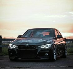 a black car parked in front of a fence with the sun going down behind it