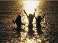 three people standing in the water with their arms up and hands raised above their heads