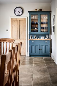 a clock is on the wall above a blue china cabinet in a kitchen with tile flooring