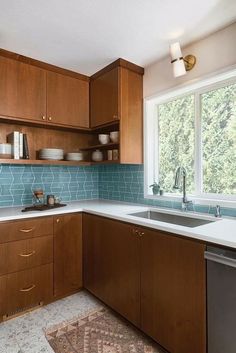 a kitchen with wooden cabinets and blue tile backsplash, white counter tops and stainless steel dishwasher