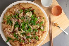 a pizza sitting on top of a white plate next to chopsticks and a cup