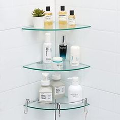 three tiered glass shelf in the corner of a white tiled wall with bottles and soaps on it