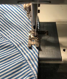 the sewing machine is working on the blue and white striped fabric