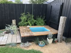 a small pool in the middle of a backyard with wooden decking and potted plants