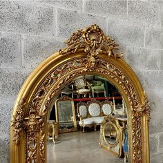 an ornate gold framed mirror sitting on top of a floor next to a brick wall