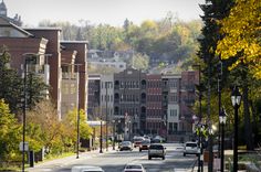 several cars are driving down the street in front of some tall buildings and trees with yellow leaves on them