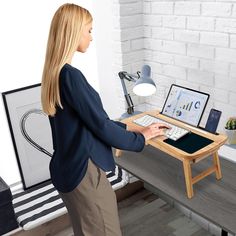 a woman standing at a desk with a laptop and keyboard on it, while looking at the screen