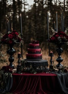 a red and black wedding cake on a table with candles in the woods behind it