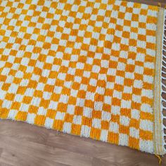 an orange and white checkered rug is laying on the floor next to a wood floor