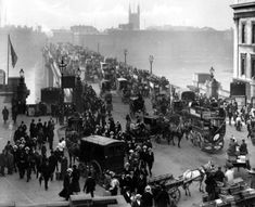 an old black and white photo of people walking on the street with horse drawn carriages