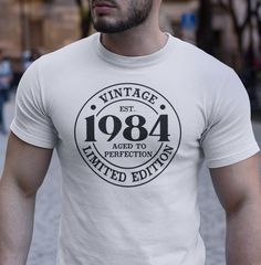 a man wearing a white t - shirt with an aged to perfection logo on it