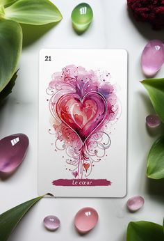 a card with a heart on it surrounded by stones and flowers, including one green leaf