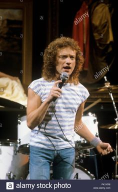 an image of a man singing into a microphone in front of a drum set - stock image