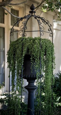 a lamp post covered in green plants and hanging from it's sides, next to a building