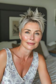 Smiling person with short, spiky hair sitting on a bed in a brightly lit room.