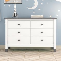 a white dresser sitting in front of a wall with stars and moon decals on it