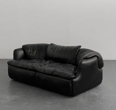 a black leather couch sitting on top of a cement floor next to a white wall