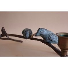 two little birds sitting on a branch next to a vase and candle holder with one bird perched on the branch