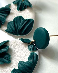 two green and white earrings with leaves on them sitting on a table next to each other