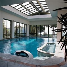 an indoor swimming pool with glass doors leading to the patio and hot tub in the center