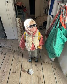 a small child wearing sunglasses and a scarf standing in front of a white refrigerator freezer