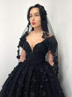 a woman wearing a black wedding dress with flowers on the skirt and veil over her head