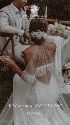 a bride and groom sitting at a table with flowers in their hair, holding wine glasses