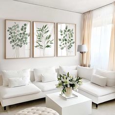 a living room with white couches and paintings on the wall above them, along with a coffee table