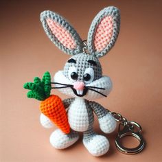 a crocheted bunny holding a carrot keychain on a pink surface with a brown background