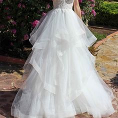 a woman in a white wedding dress standing on a stone path with flowers behind her