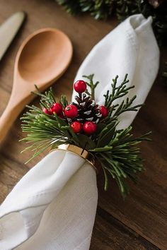 napkins with pine cones and berries are sitting on a wooden table next to utensils