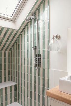 a green and white tiled bathroom with skylight above the shower head, toilet and sink