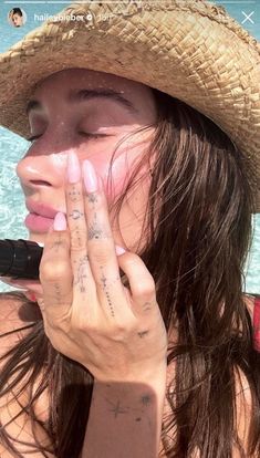 a woman wearing a straw hat and holding her hand up to her face while standing in the water