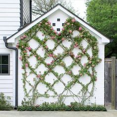 a white building with pink flowers growing on it's side and a wooden fence behind it