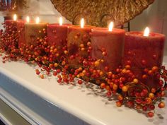 candles are lined up on a mantle with berries