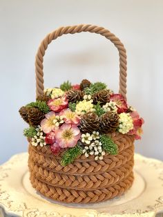 a basket with flowers and pine cones sitting on top of a white tablecloth covered cake